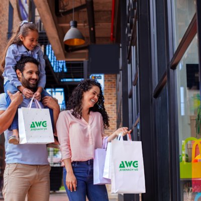 Familie mit einem Kind steht mit AWG-Tüten vor einem Geschäft