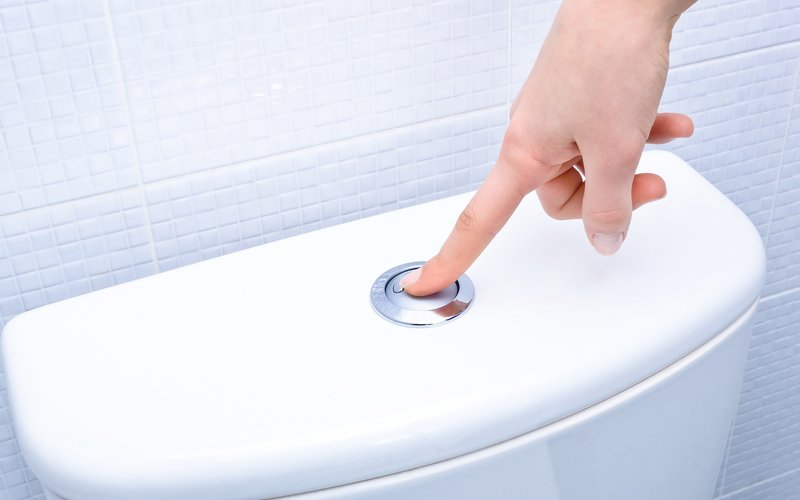 Finger betätigt die Spülung einer Toilette